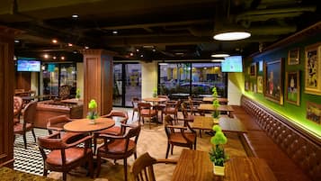 A restaurant with wooden tables and chairs, a checkered floor, and a green wall with framed pictures.