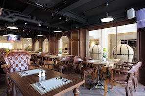 Un restaurante con mesas de madera y sillas de cuero, ventanas amplias y una pantalla de televisión.