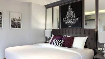 A large bed with a dark headboard, white bedding, and multiple pillows. There are framed pictures on the wall and a chandelier above the bed.