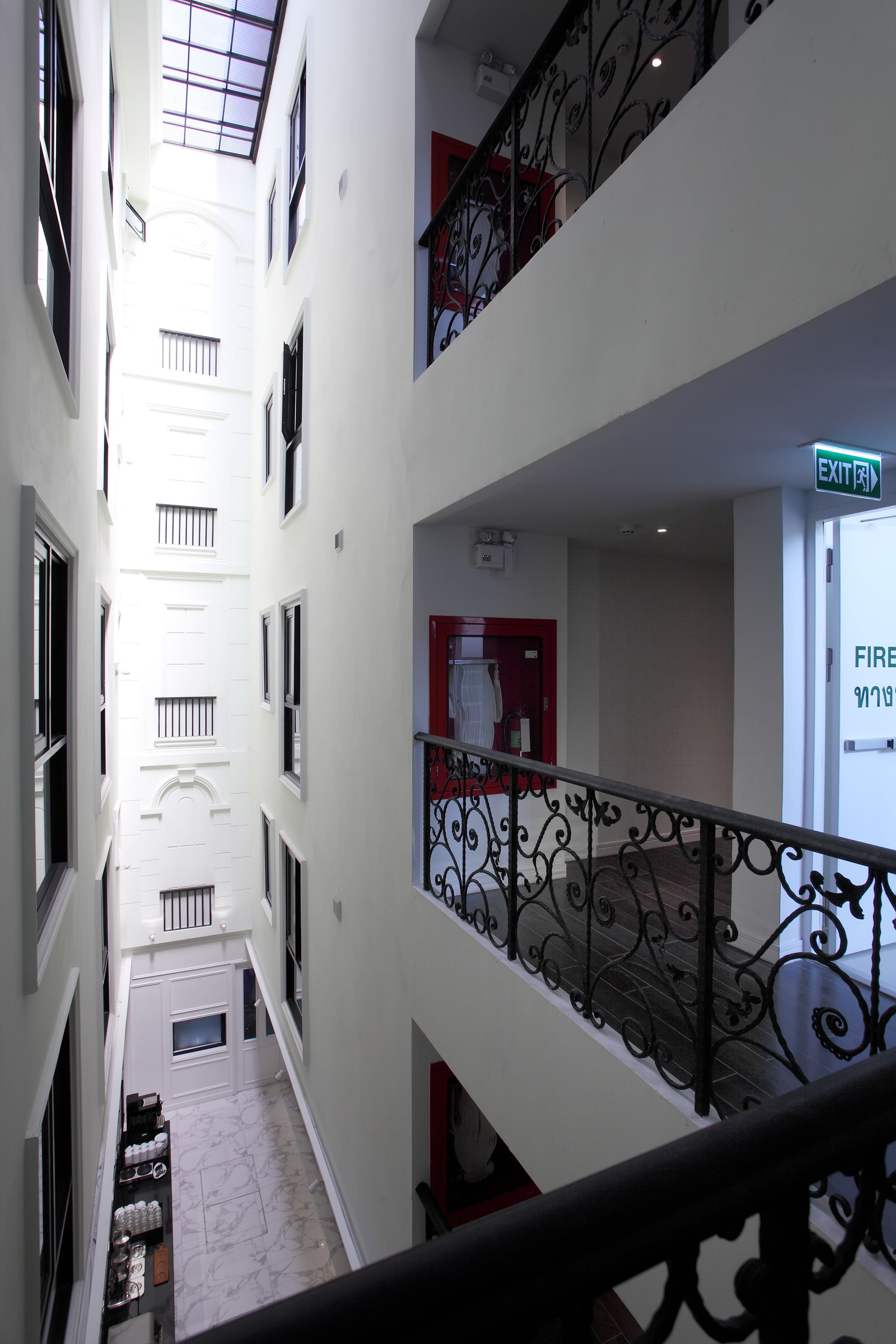 A multi-level interior with a central corridor, metal railings, and a fire exit sign.