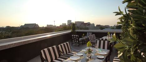 A rooftop dining area with striped seating and a table set for four, overlooking a cityscape.