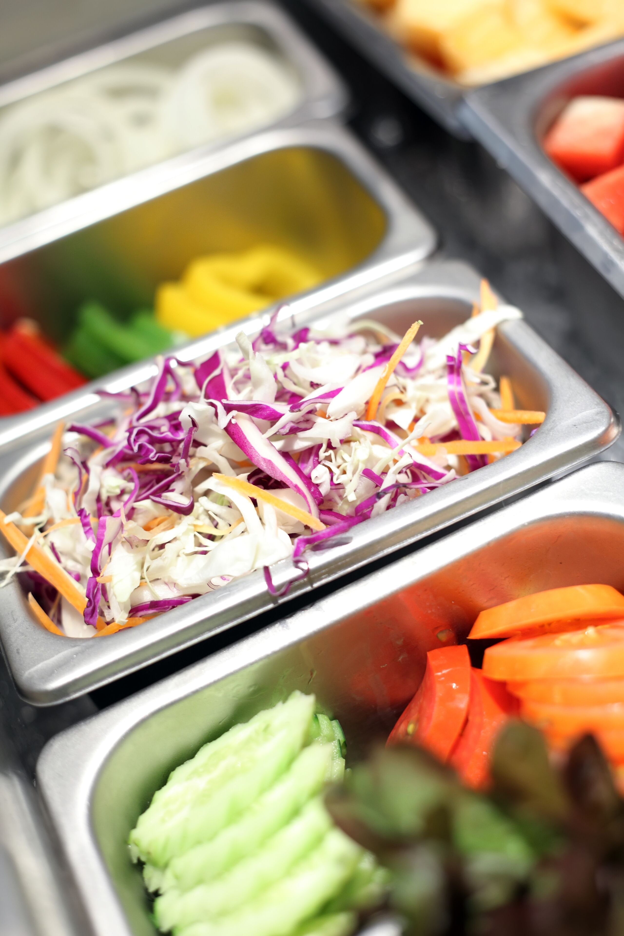 Un bufé con diferentes opciones de comida, incluyendo ensalada de col, zanahorias y otras verduras.
