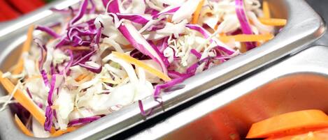 Un bufé con diferentes opciones de comida, incluyendo ensalada de col, zanahorias y otras verduras.