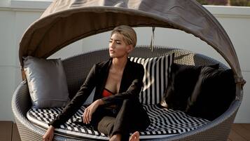 A person seated in a round, woven outdoor chair with a canopy, on a wooden deck with a cityscape in the background.
