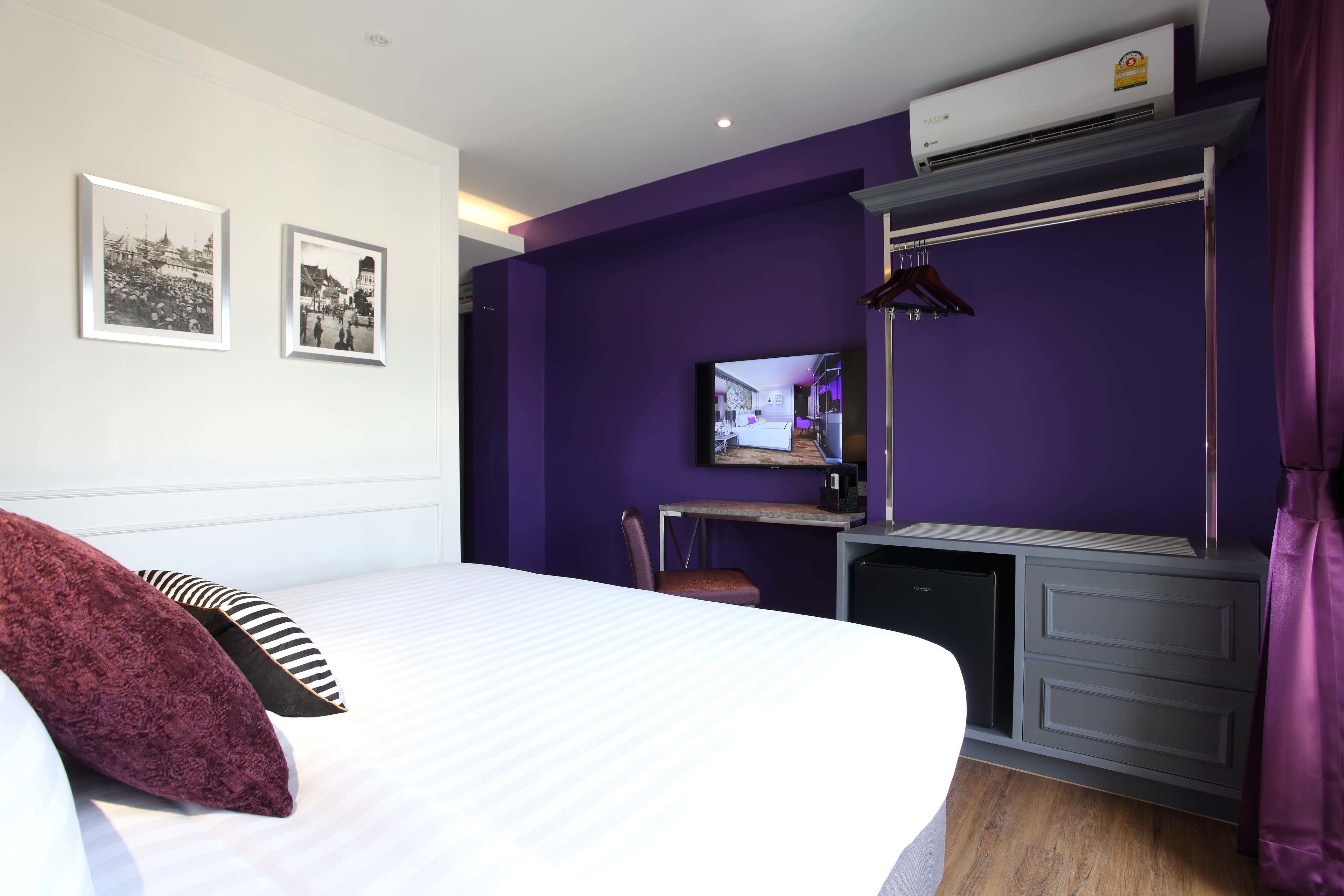 A hotel room with a bed, a desk with a computer, a television, and two framed pictures on the wall.