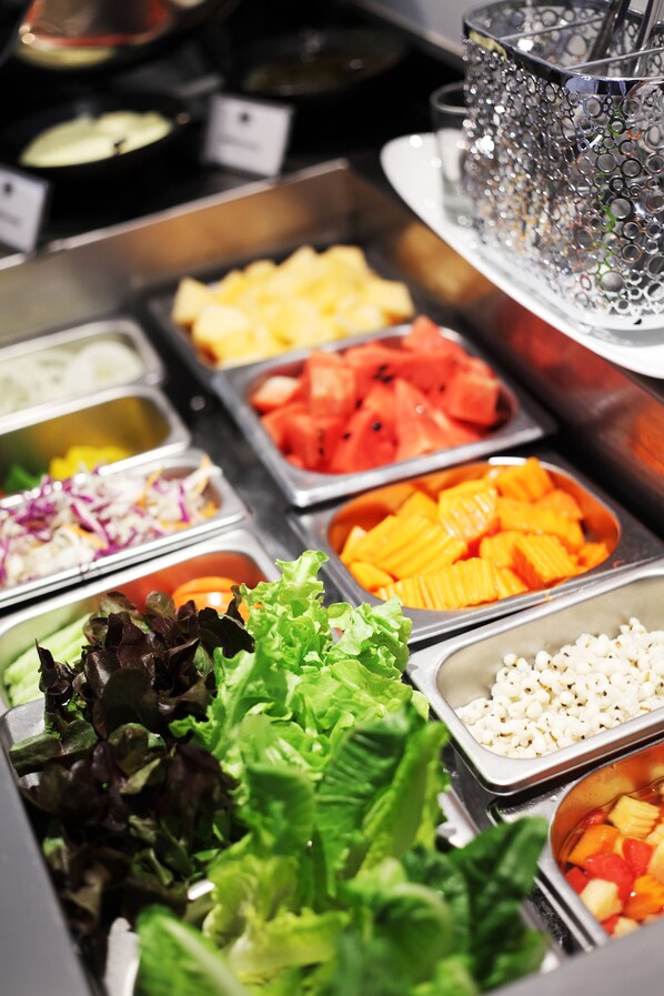 Un bufé con diversas opciones de comida, incluyendo frutas, verduras y ensaladas.
