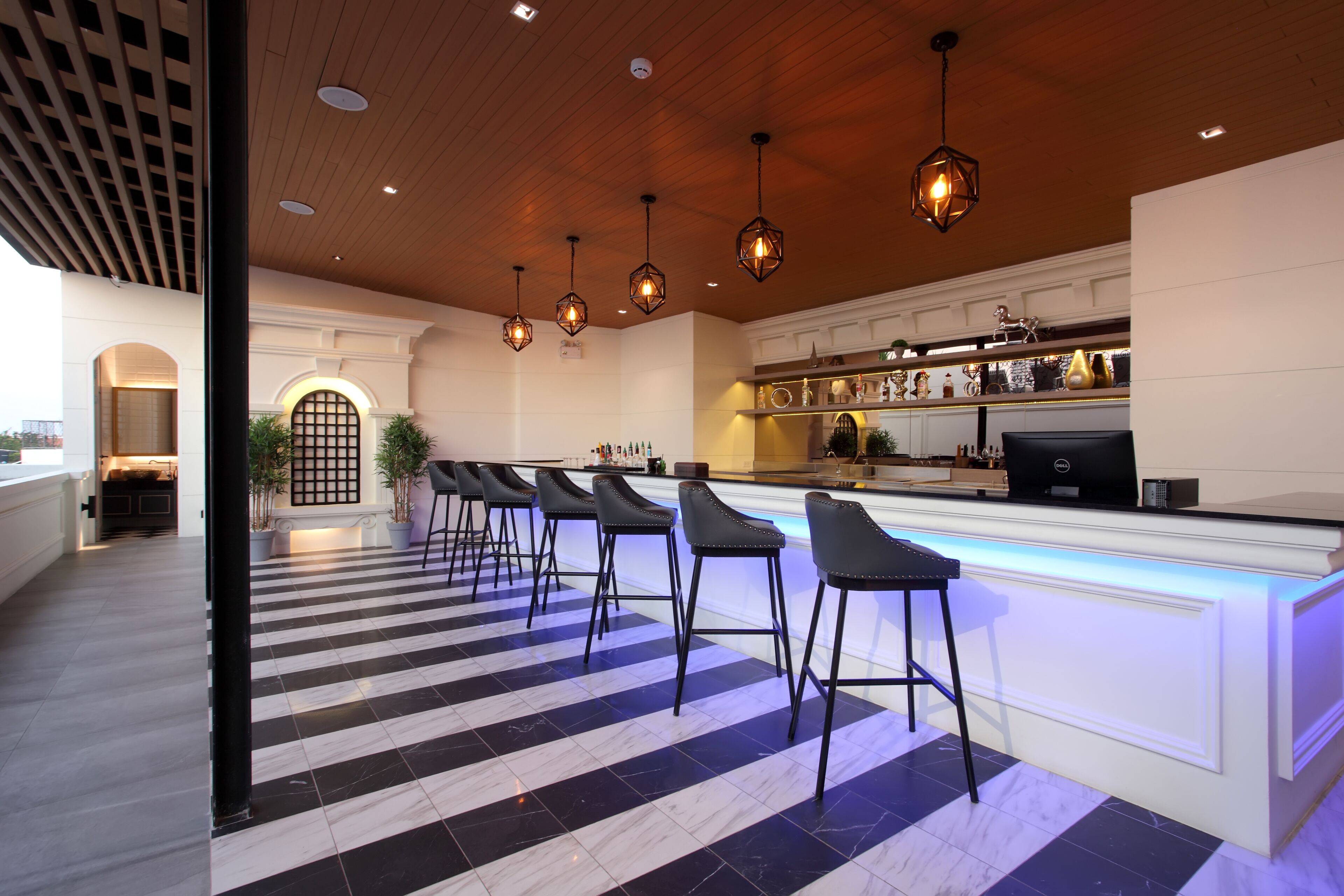Un área de bar moderna con suelo de cuadros, taburetes y lámparas colgantes.