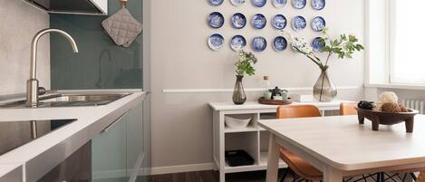 A modern kitchen with a stainless steel sink, a white countertop, and a dining area with a table and chairs.