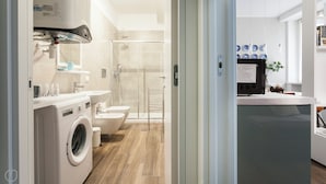 Een moderne badkamer met een wasmachine, toilet en douchecabine van glas.