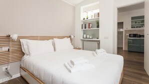 Een moderne slaapkamer met een houten hoofdbord, witte beddengoed, een bedlampje en een netjes opgemaakt bed met gevouwen handdoeken.