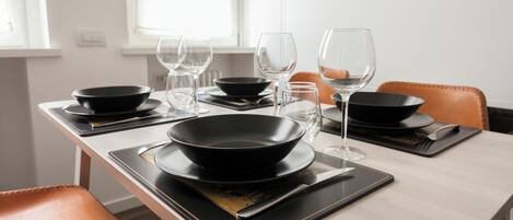 A dining table set with black bowls, wine glasses, and cutlery on black placemats.