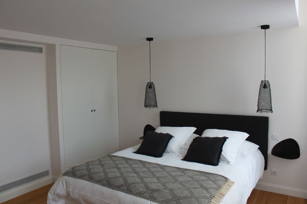 Un dormitorio con cama, dos lámparas colgantes, un armario y un calentador de pared.