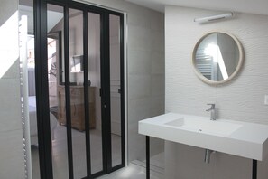 Sink and round mirror in a bathroom with a textured patterned wall and a door leading to another room.