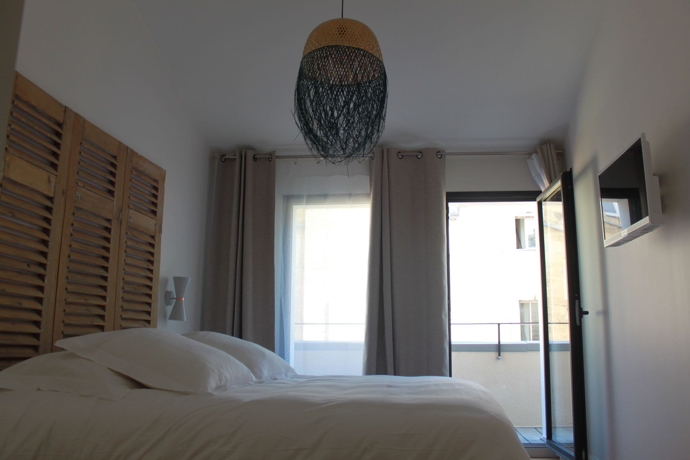 Een slaapkamer met een bed, een hanglamp, een raam met gordijnen en uitzicht op het buiten.
