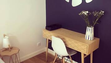 Une chambre moderne avec un bureau en bois, une chaise blanche et un vase de fleurs posé sur un mur foncé.