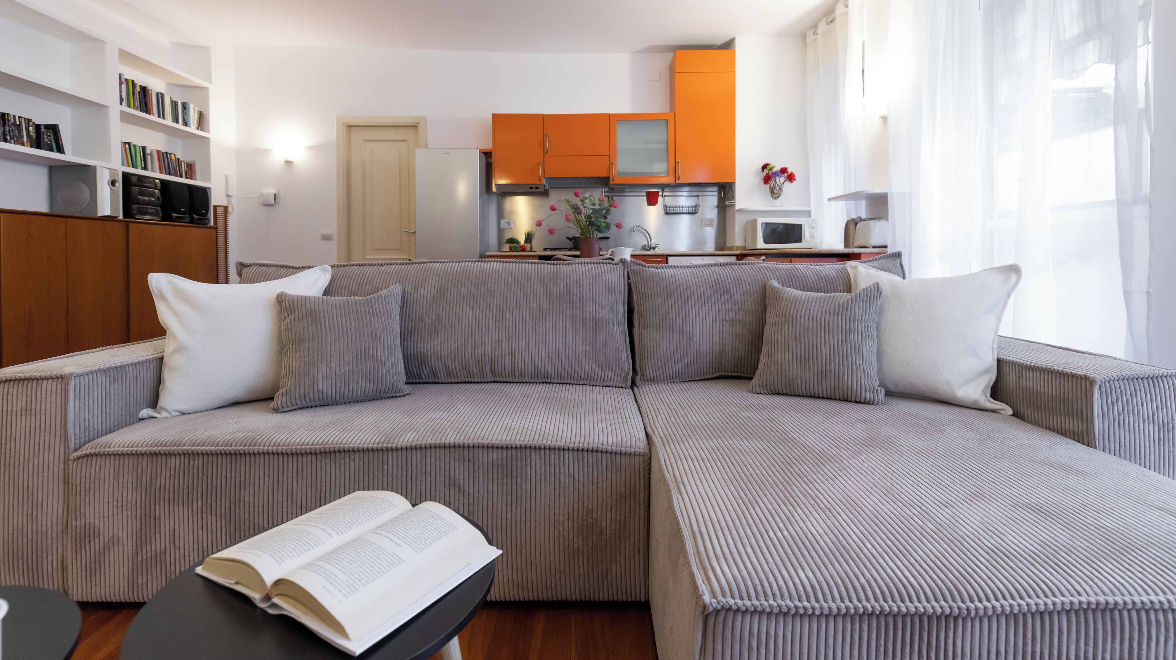 A living room with a sofa, a coffee table with a book, and a kitchen in the background.