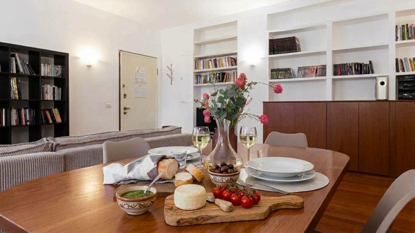 A dining area with a wooden table set for a meal, surrounded by bookshelves and a sofa.