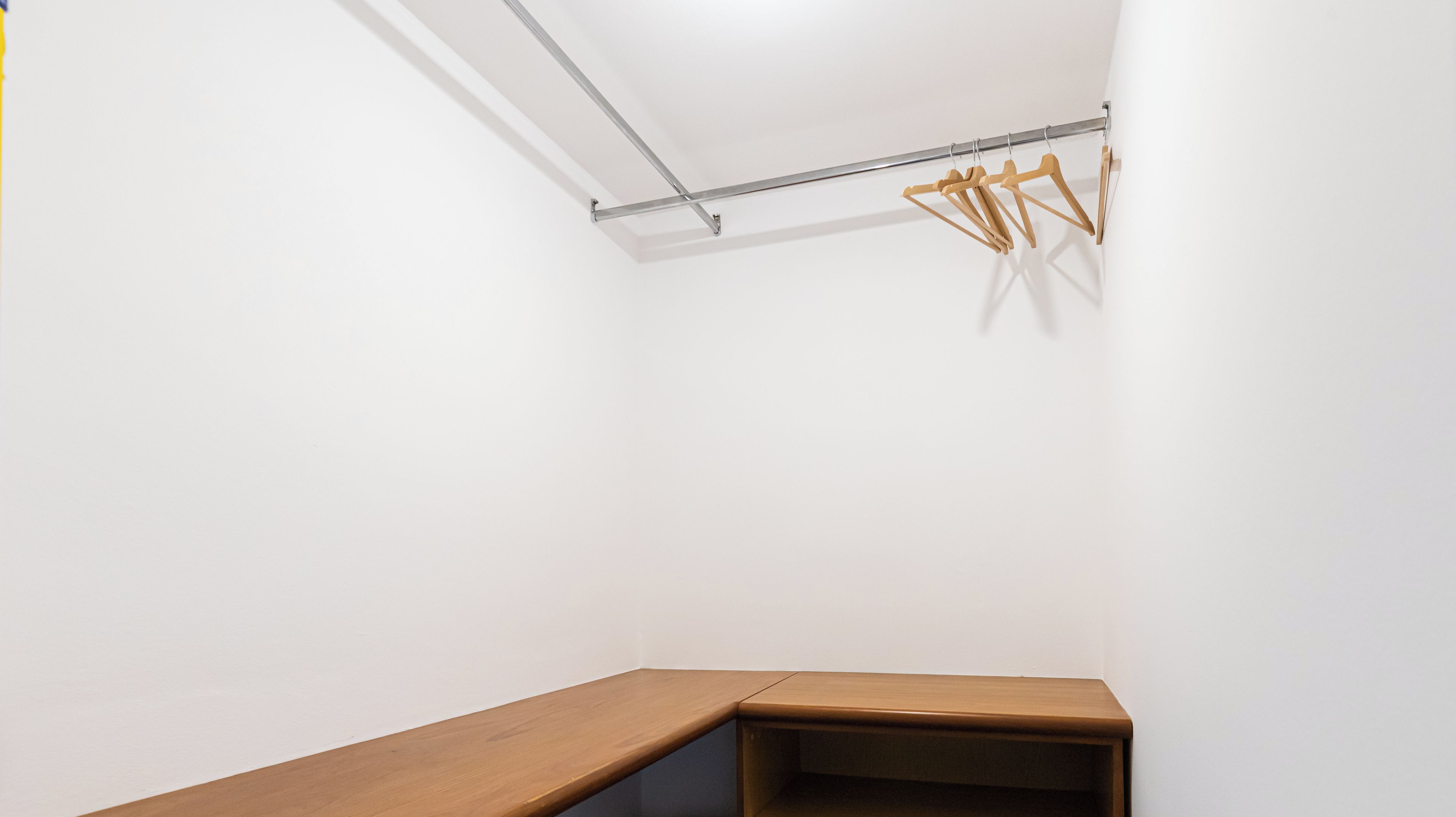 A corner of a room with a wooden bench and a metal rack with wooden hangers.