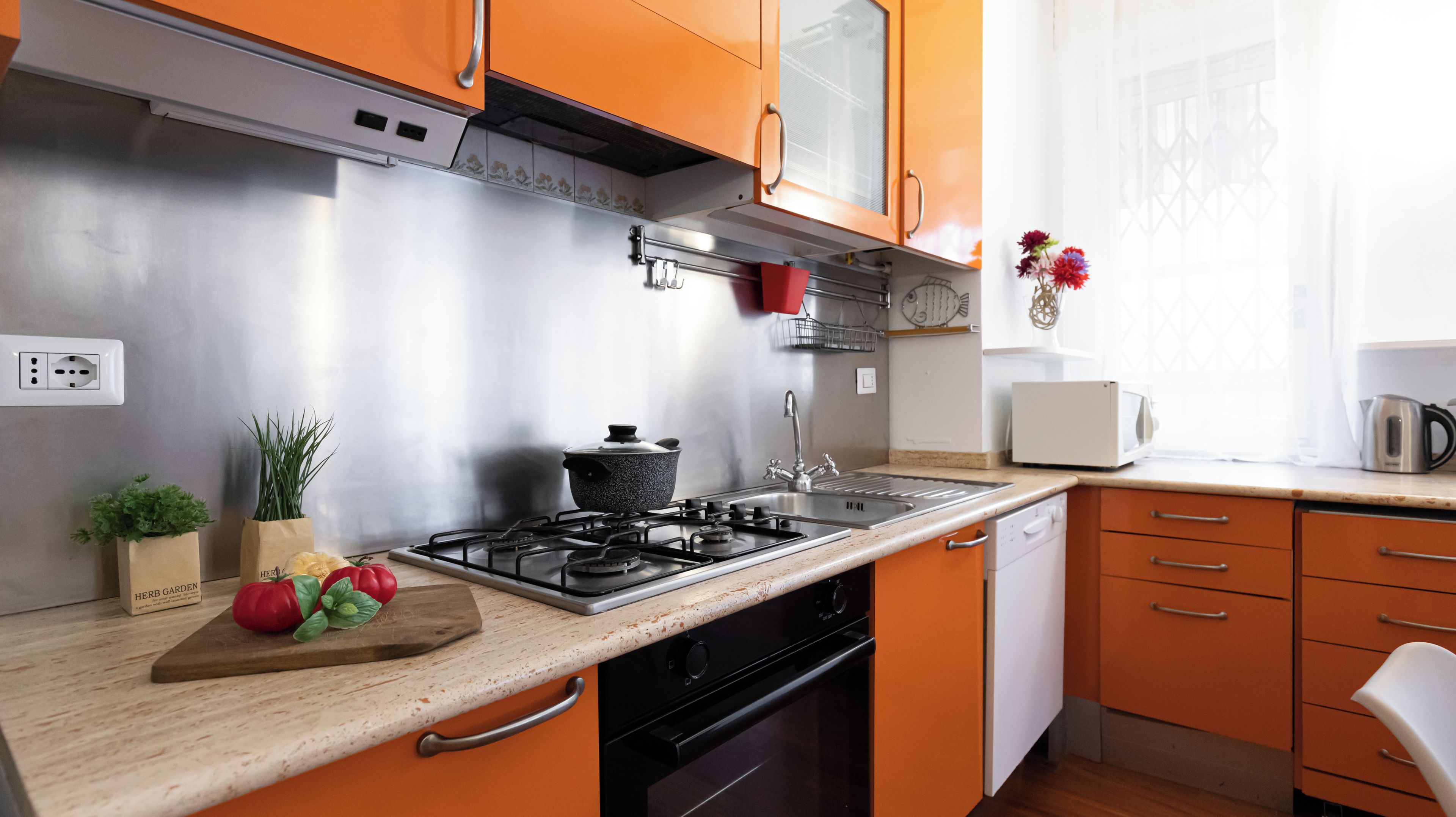 Een keuken met een fornuis, spoelbak en kasten. Op het aanrecht staat een snijplank met groenten en een pan.