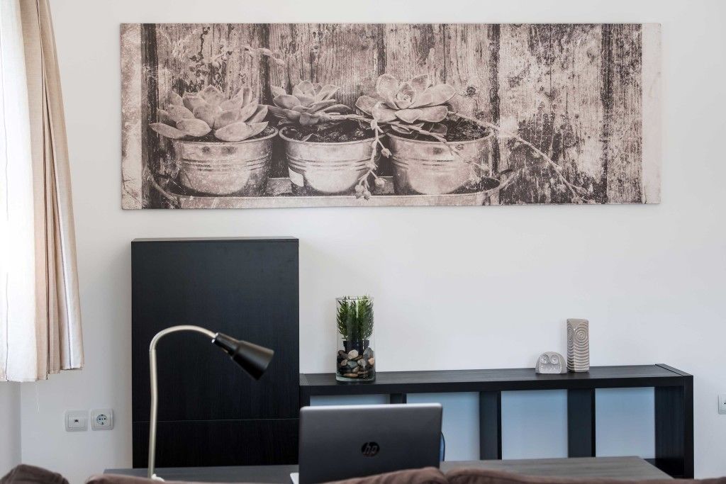 Ein modernes Zimmer mit einem großen Schwarzweiß-Kunstwerk von Topfpflanzen, einem Schreibtisch mit einem Laptop, einer Lampe und einer kleinen Zimmerpflanze auf einem Regal.