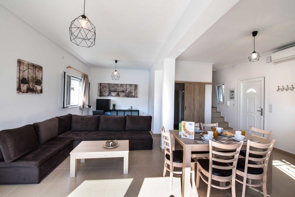 Un salon moderne avec un canapé d’angle marron foncé, une table basse blanche et un coin repas comprenant des chaises en bois et une table mise pour le petit-déjeuner.