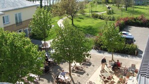 A courtyard with outdoor seating, a lake view, and a building with a sloped roof. - Zum Rittmeister (Werder (Havel))