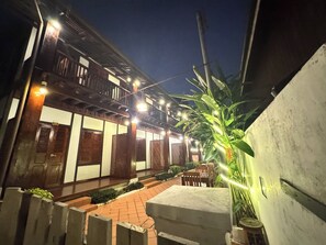 A courtyard with a wooden building, outdoor seating, and a large plant. - Villa Kee Lee Hotel (Luang Prabang)