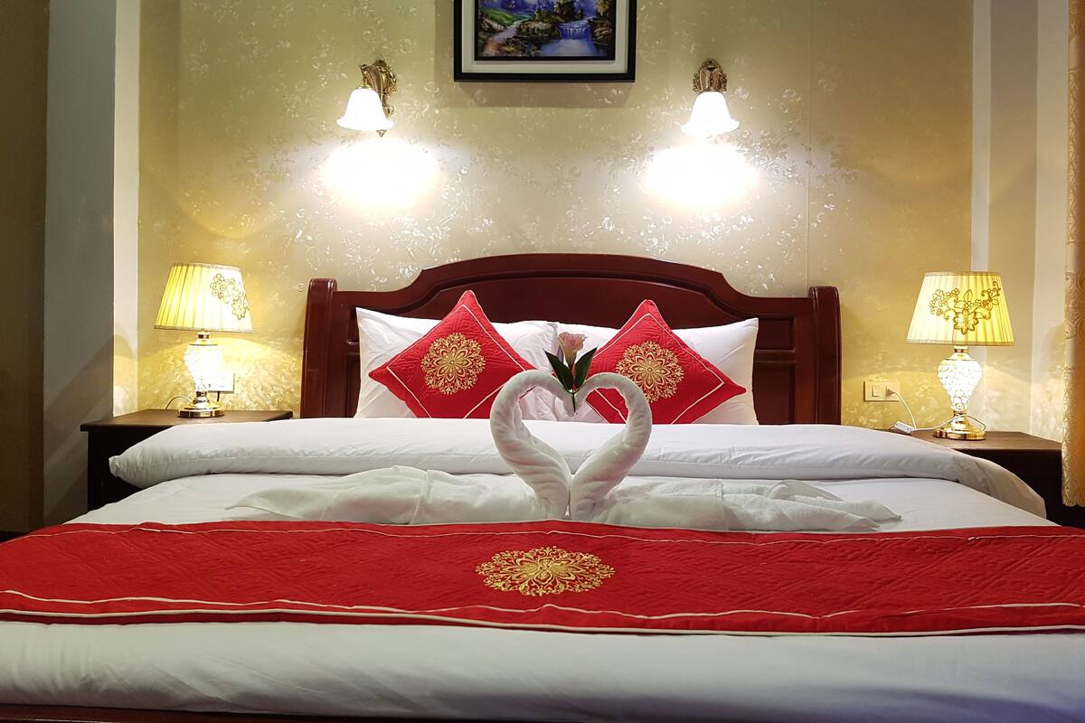 A hotel room with a neatly made bed, two bedside lamps, and a framed picture on the wall.