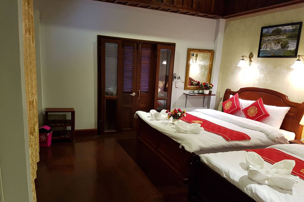 A hotel room with two beds, a wooden headboard, a nightstand with a lamp, a mirror, and a picture on the wall.