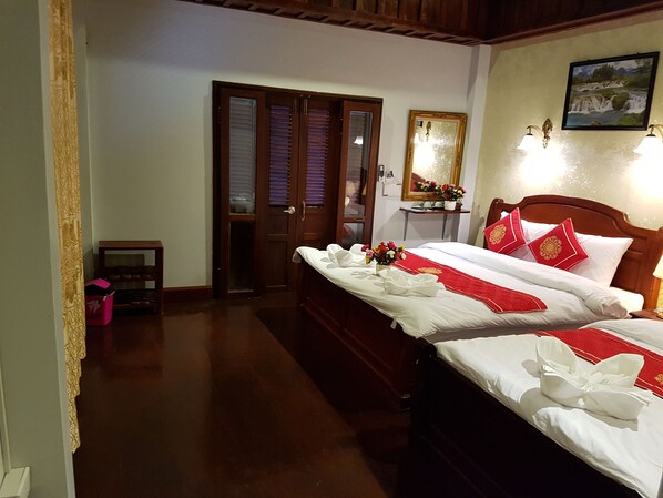 A hotel room with two beds, a wooden headboard, a nightstand with a lamp, a mirror, and a picture on the wall. - Villa Kee Lee Hotel (Luang Prabang)