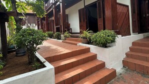 Een traditioneel houten gebouw met balkon, treden naar een deur en bloempotten.