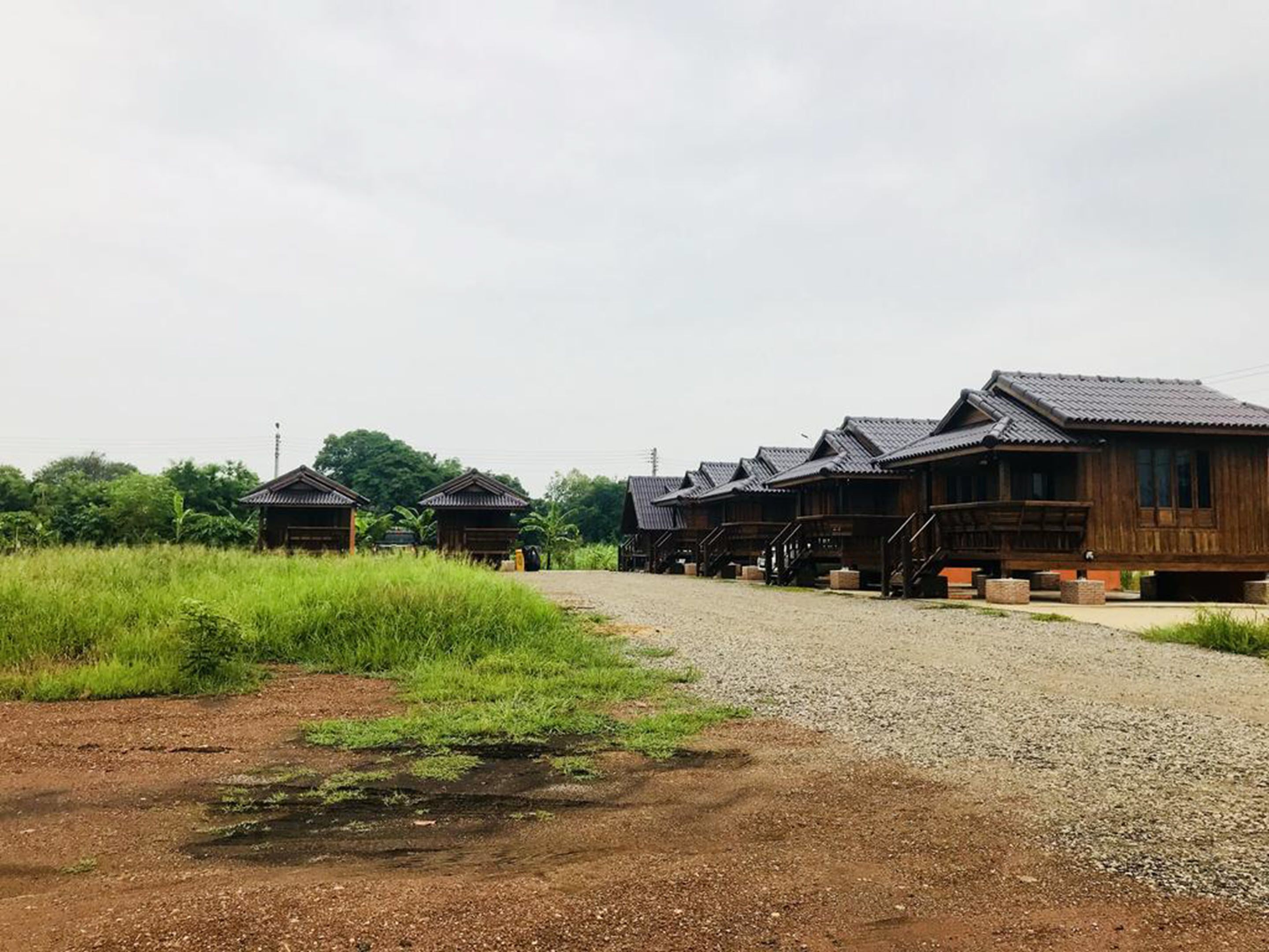 A row of traditional wooden cabins with a gravel path leading to them, surrounded by greenery.