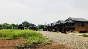 A row of traditional wooden cabins with a gravel path leading to them, surrounded by greenery.