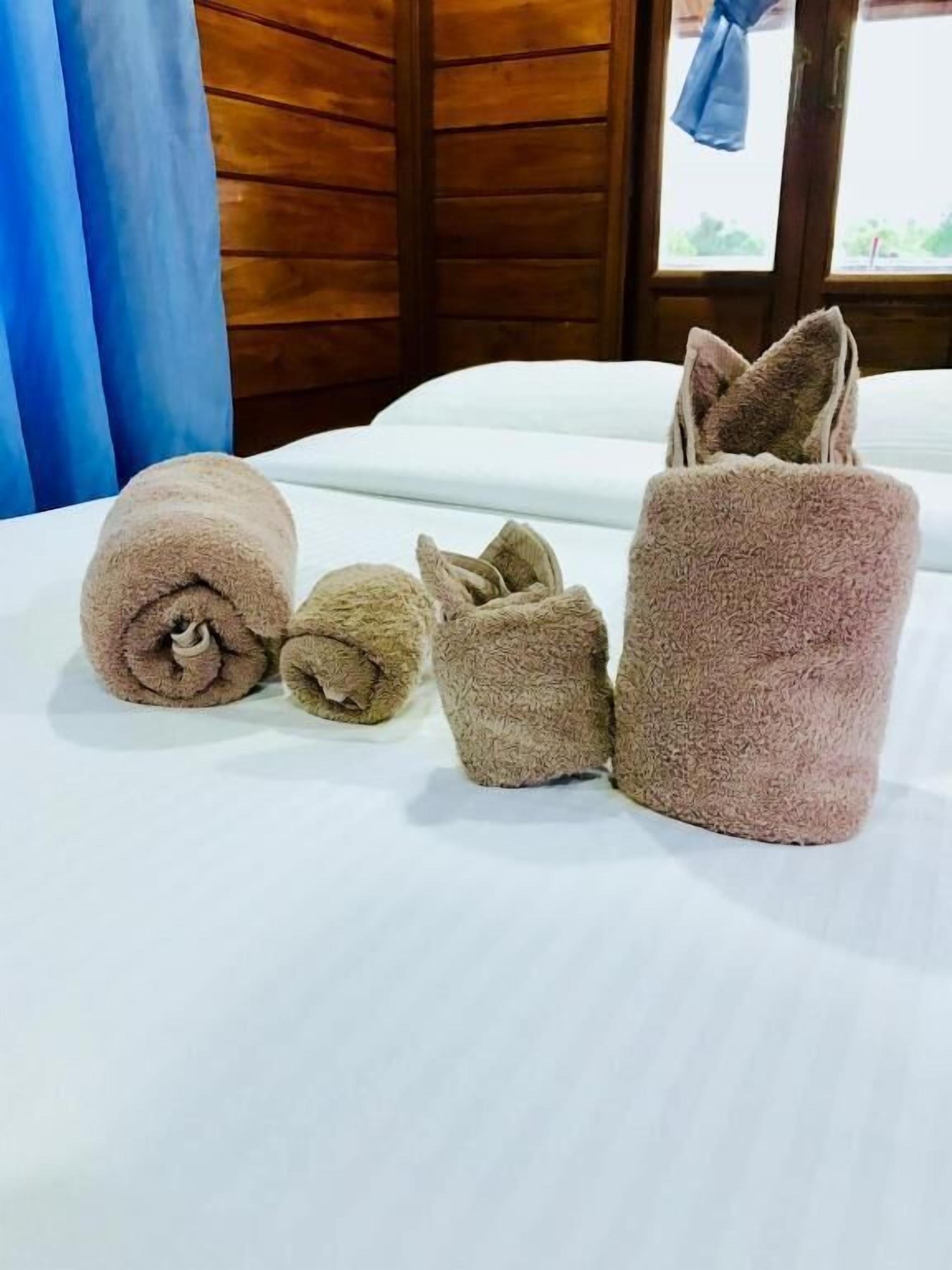 Uma cama com lençóis brancos e quatro toalhas enroladas em diferentes tamanhos e cores.