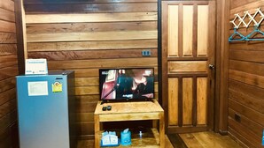 A room with wooden paneling, a television on a wooden table, a refrigerator, and a door with a coat rack. - We Care Resort (Wichian Buri)