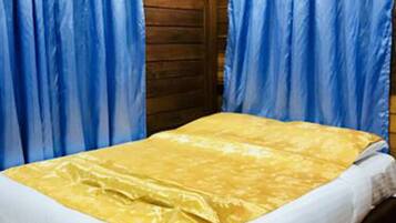 A single bed with a yellow bedspread and white pillows in a wooden room with blue curtains.