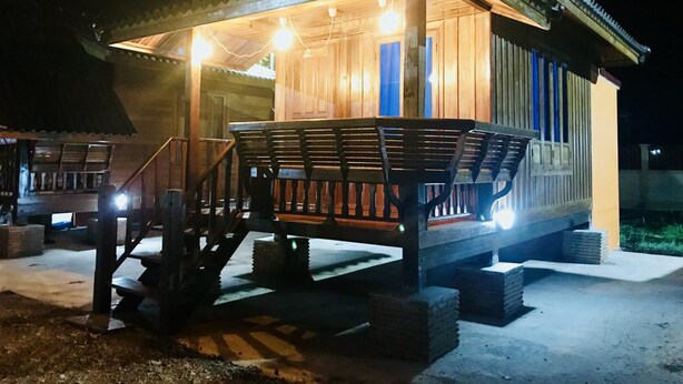 A wooden cabin with a porch, steps, and a railing. - We Care Resort (Wichian Buri)