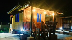 A wooden cabin with a porch, steps, and a chair. - We Care Resort (Wichian Buri)