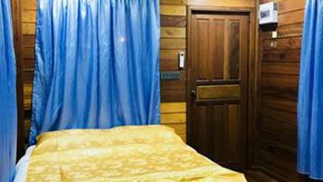 A bedroom with a wooden floor, a bed with a white and yellow bedspread, and blue curtains.