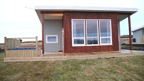 A modern single-story building with a large window, a wooden deck, and a covered porch area. - Blue View Cabin 4A with Hot Tub (Bláskógabyggd)