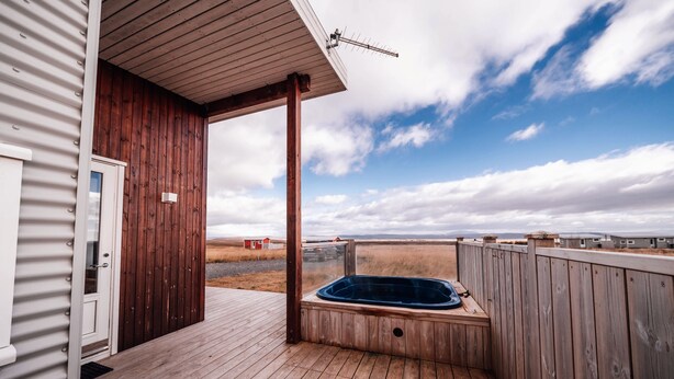 A wooden deck with a hot tub, a door, and a view of the landscape. - Blue View Cabin 4A with Hot Tub (Bláskógabyggd)