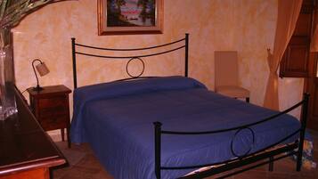 Una camera da letto con un letto, un comodino, una lampada, una sedia, un vaso con fiori e un quadro appeso al muro.