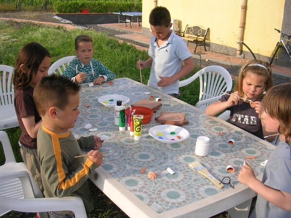 A group of children engaged in a craft activity outdoors at a table with mosaic tiles.
