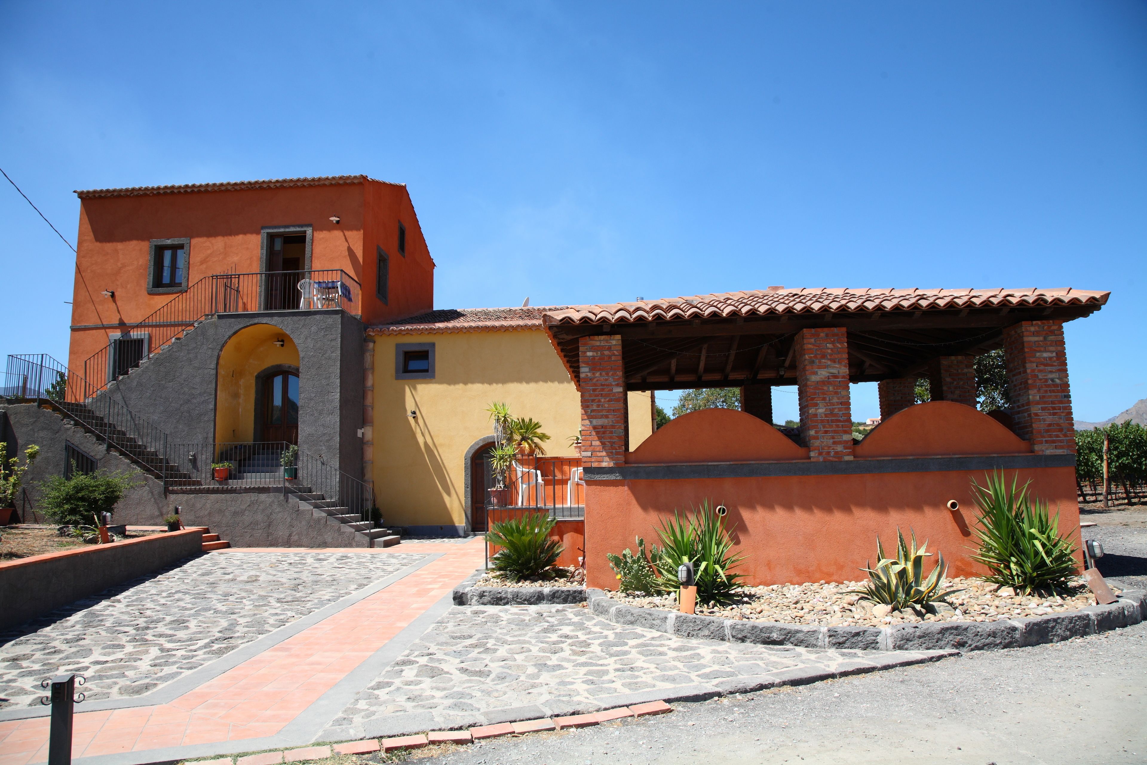 A two-story building with a yellow facade, a red-tiled roof, and a stone-paved courtyard.