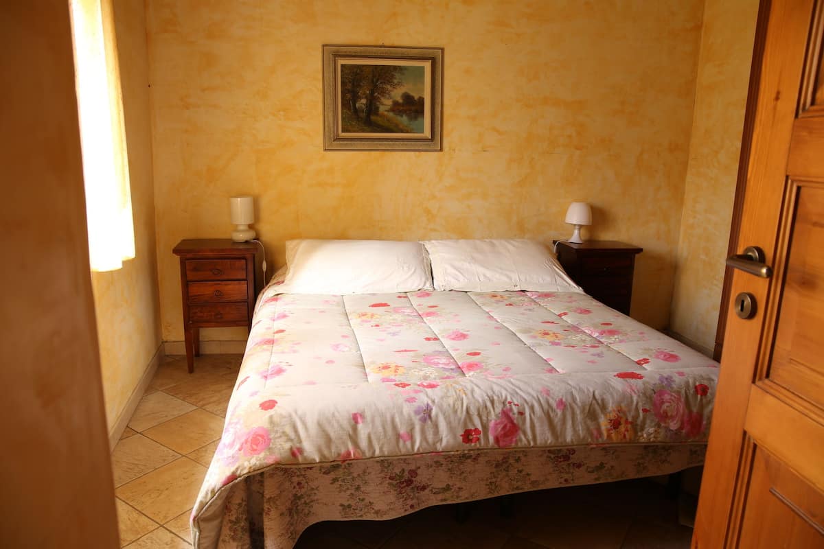 Ein Schlafzimmer mit einem Bett, zwei Nachttischen, einem Schreibtisch und einem gerahmten Bild an der Wand sowie einer Tür.
