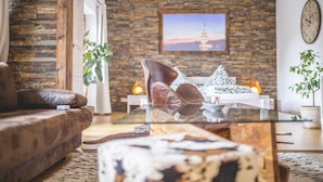 Un salon avec un mur en pierre, un canapé, une table basse en verre et un tableau représentant un coucher de soleil.