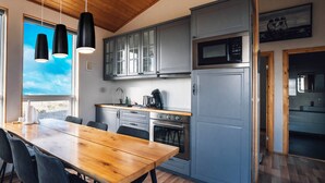 A modern kitchen with grey cabinets, a wooden dining table, and black pendant lights. - Blue View Cabin 5A with Hot Tub (Bláskógabyggd)