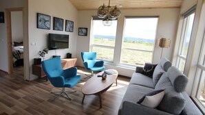 A modern living room with a grey sofa, blue armchairs, a wooden coffee table, and a TV mounted on the wall. - Blue View Cabin 5A with Hot Tub (Bláskógabyggd)