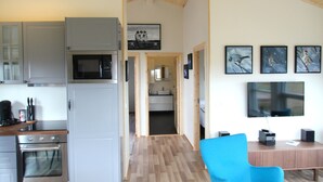 A modern kitchen with grey cabinets, a microwave, and an oven. There is a blue chair and a wooden table in the living area. - Blue View Cabin 5A with Hot Tub (Bláskógabyggd)