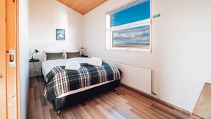 A bedroom with a bed, a window with a view, a radiator, and a wooden floor. - Blue View Cabin 5A with Hot Tub (Bláskógabyggd)